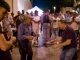 Felici & Conflenti, ballo notturno in un vicolo di pietra: un anziano con la coppola danza davanti a un altro uomo, accanto a un giovane che suona uno strumento a corde; intorno la gente in cerchio, qualcuno riprende col telefono.