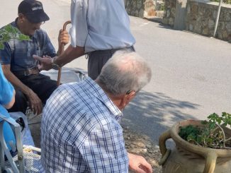 Tre anziani conversano seduti all'ombra in un angolo di piazza a Martirano Lombardo, con alle spalle una casa dal tetto in tegole rosse