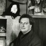 Carlo Levi in posa davanti a una scultura di testa femminile e a un dipinto con figure anziane