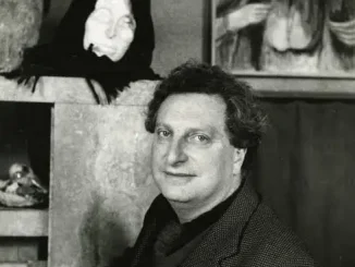 Carlo Levi in posa davanti a una scultura di testa femminile e a un dipinto con figure anziane