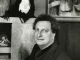 Carlo Levi in posa davanti a una scultura di testa femminile e a un dipinto con figure anziane